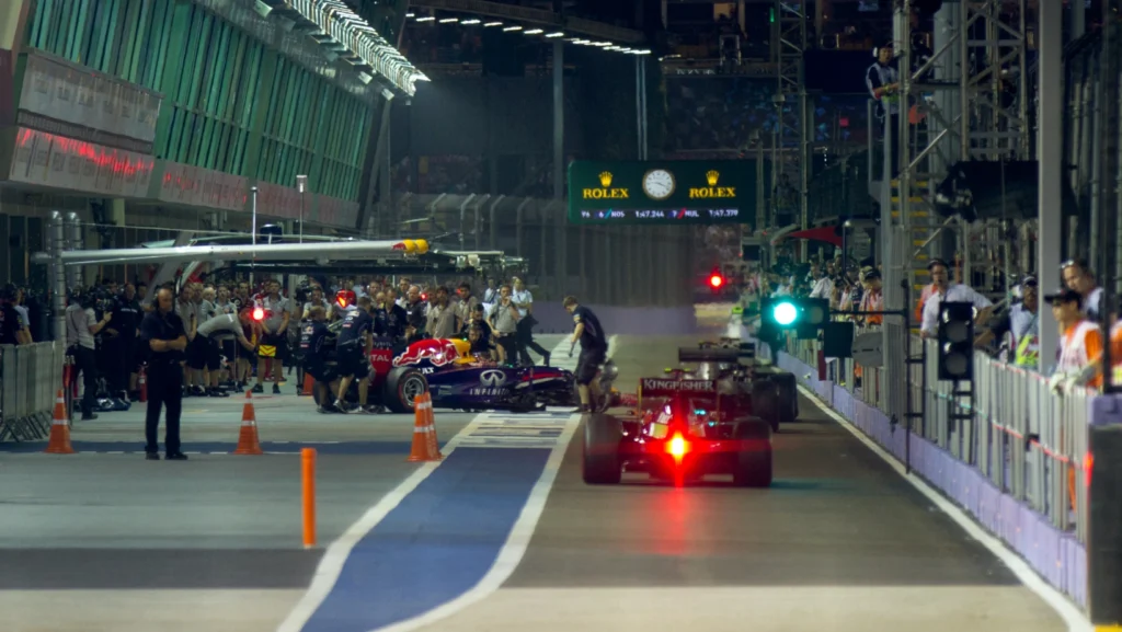 Formula 1 cars in the pit lane during the Singapore Grand Prix, with teams performing rapid tire changes.